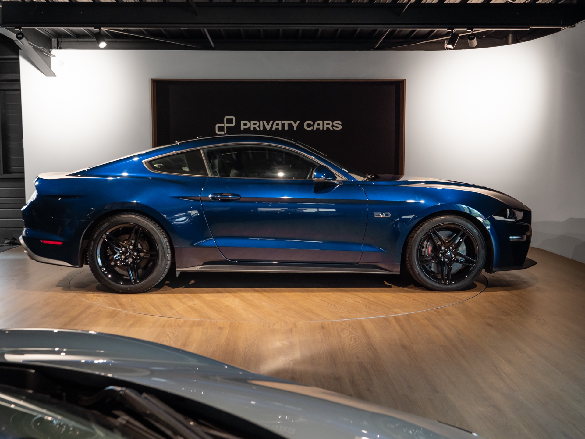 Vue latérale avec jantes noires – PORSCHE – Ford Mustang V8 – 2019 – Bleu Kona – 48 900 km – 450 ch – V8 Atmo – Transmission : Manuelle – Origine France – Privaty Cars – Dépôt-vente de véhicules PORSCHE près de Niort